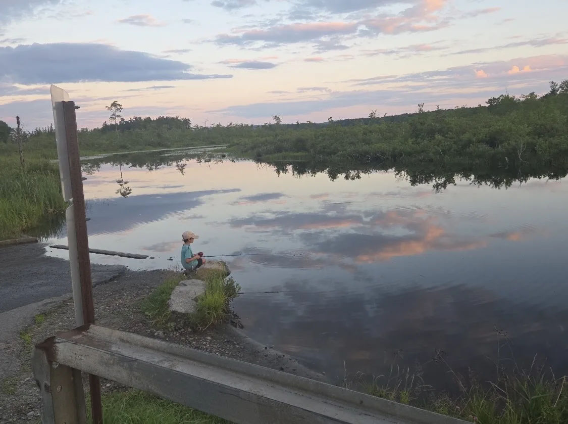 A child fishing beside calm water at sunset